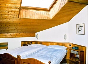 Un dormitorio con tragaluz, techo de madera, cama, mesitas de noche y un cuadro enmarcado en la pared.