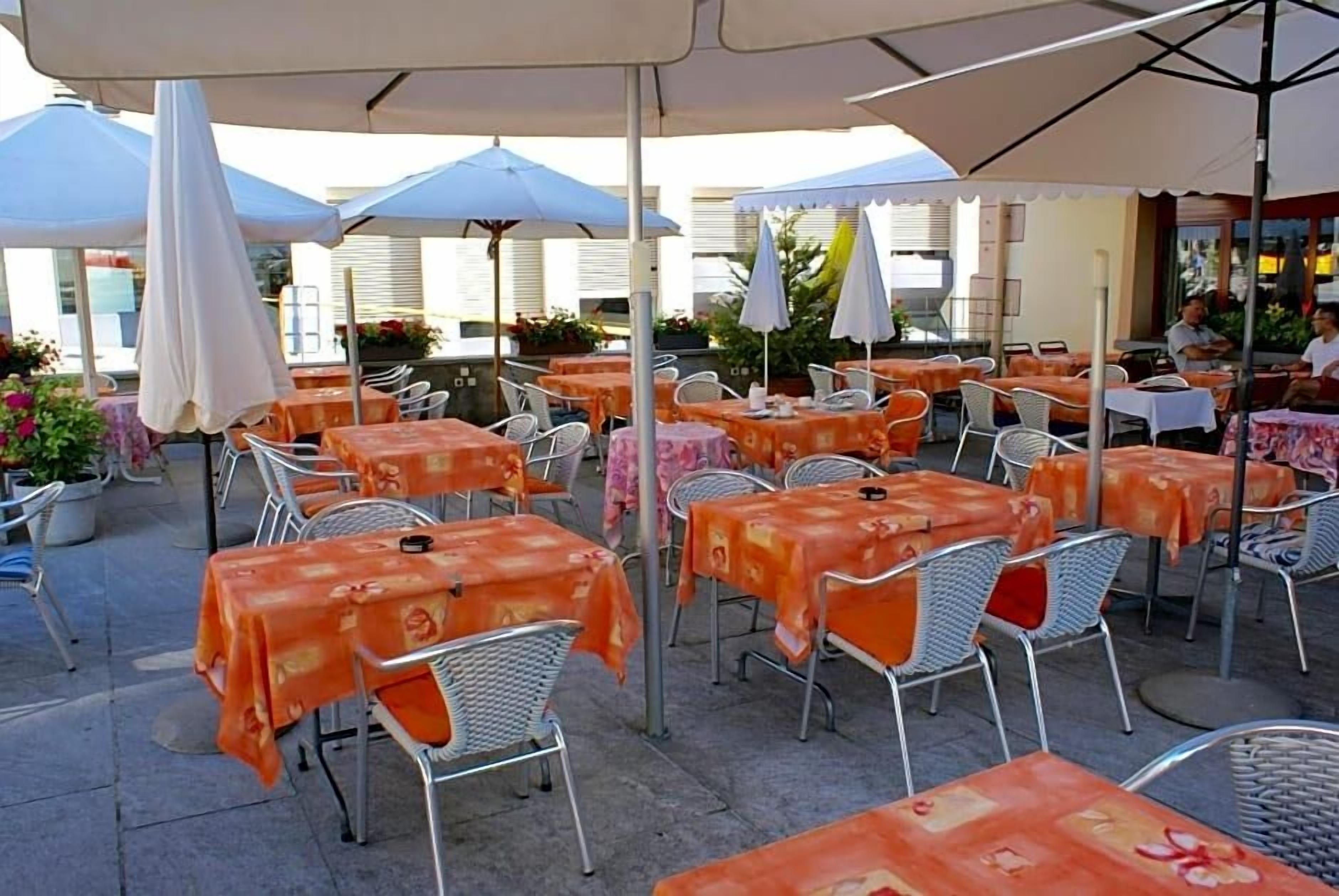 An outdoor café with tables and chairs, covered by umbrellas, and a building in the background.