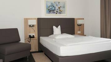 A hotel room with a bed, a sofa, a bedside table with a lamp, a phone, and a painting on the wall.