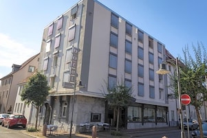 Un hotel de varios pisos con fachada moderna, mobiliario exterior y un letrero de 'prohibido el acceso'.