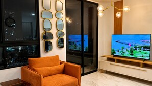 Un salon moderne avec un canapé, un téléviseur posé sur un meuble en bois et une vue sur la ville par la fenêtre.