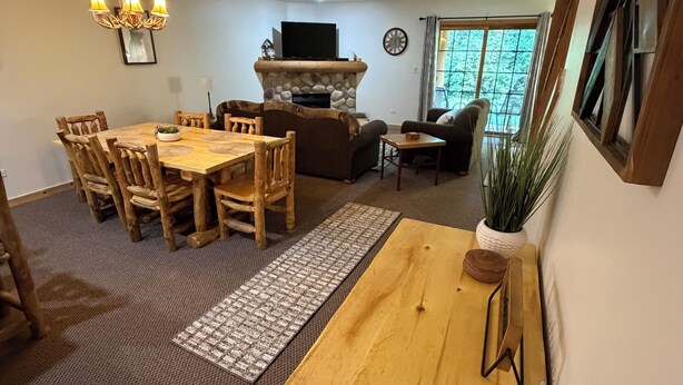 Una sala de estar con una mesa de comedor de madera, sillas, chimenea, televisor y un ventanal grande.