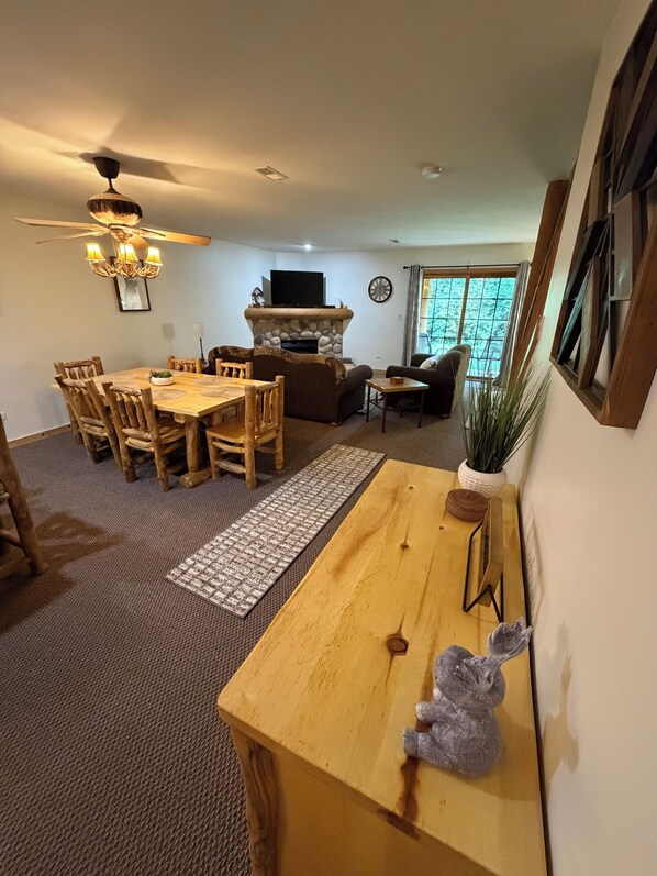 A living room with a wooden dining table, chairs, a fireplace, a television, and a large window.