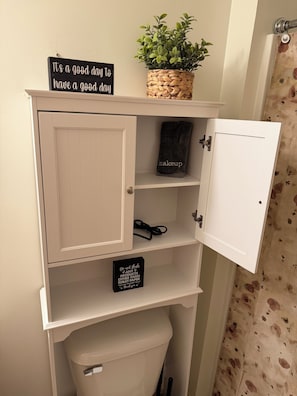 A bathroom vanity with a sign saying 'It's a good day to have a good day,' a potted plant, a makeup bag, and a sign instructing not to flush anything but toilet paper.