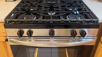 A stainless steel kitchen with a gas stove, oven, and a digital display.
