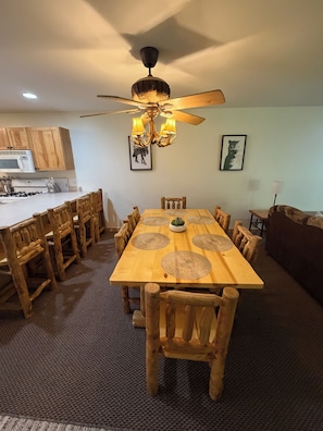 A dining area with a wooden table and chairs, a ceiling fan, and a kitchen in the background.