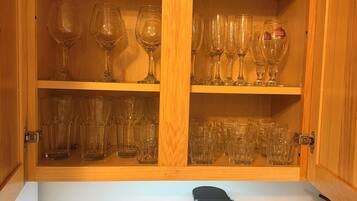 Un meuble en bois, doté d’étagères où sont rangés divers objets en verre, et une machine à café posée sur le plan de travail en dessous.