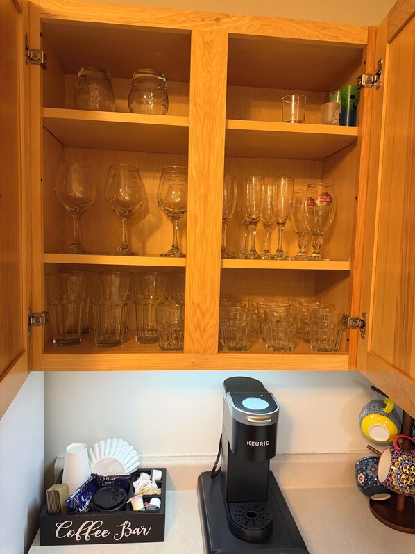 Un mueble de madera con estantes que contiene diferentes vasos y una cafetera sobre la encimera.