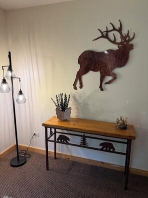 A room with a wooden console table, a wall-mounted deer sculpture, a floor lamp, and a potted plant.