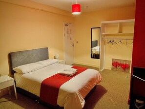 Hotellihuone, jossa on sänky, yöpöytä, vaatekaappi ja peili.