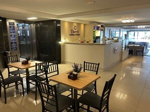 Um restaurante com mesas, cadeiras, um balcão e uma placa que diz 'Cerri CAFETERIA & DOCERIA'.