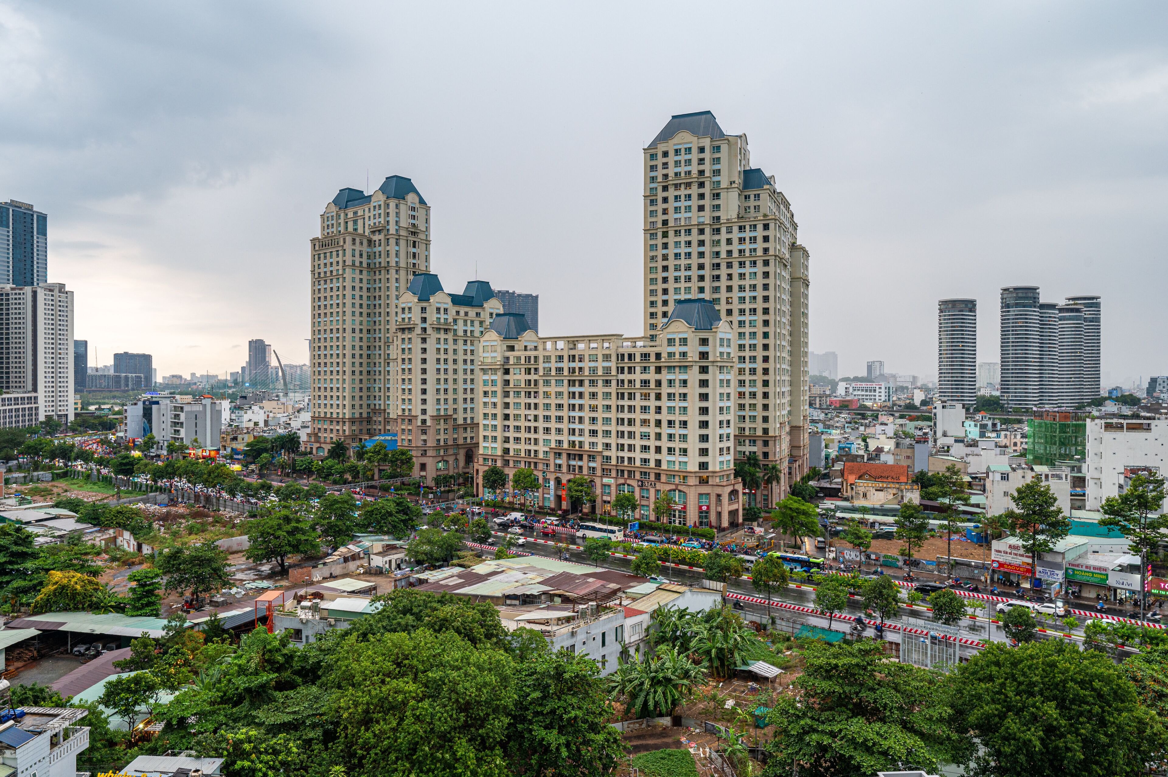 Un edificio grande con varios pisos, rodeado de otros edificios y árboles.