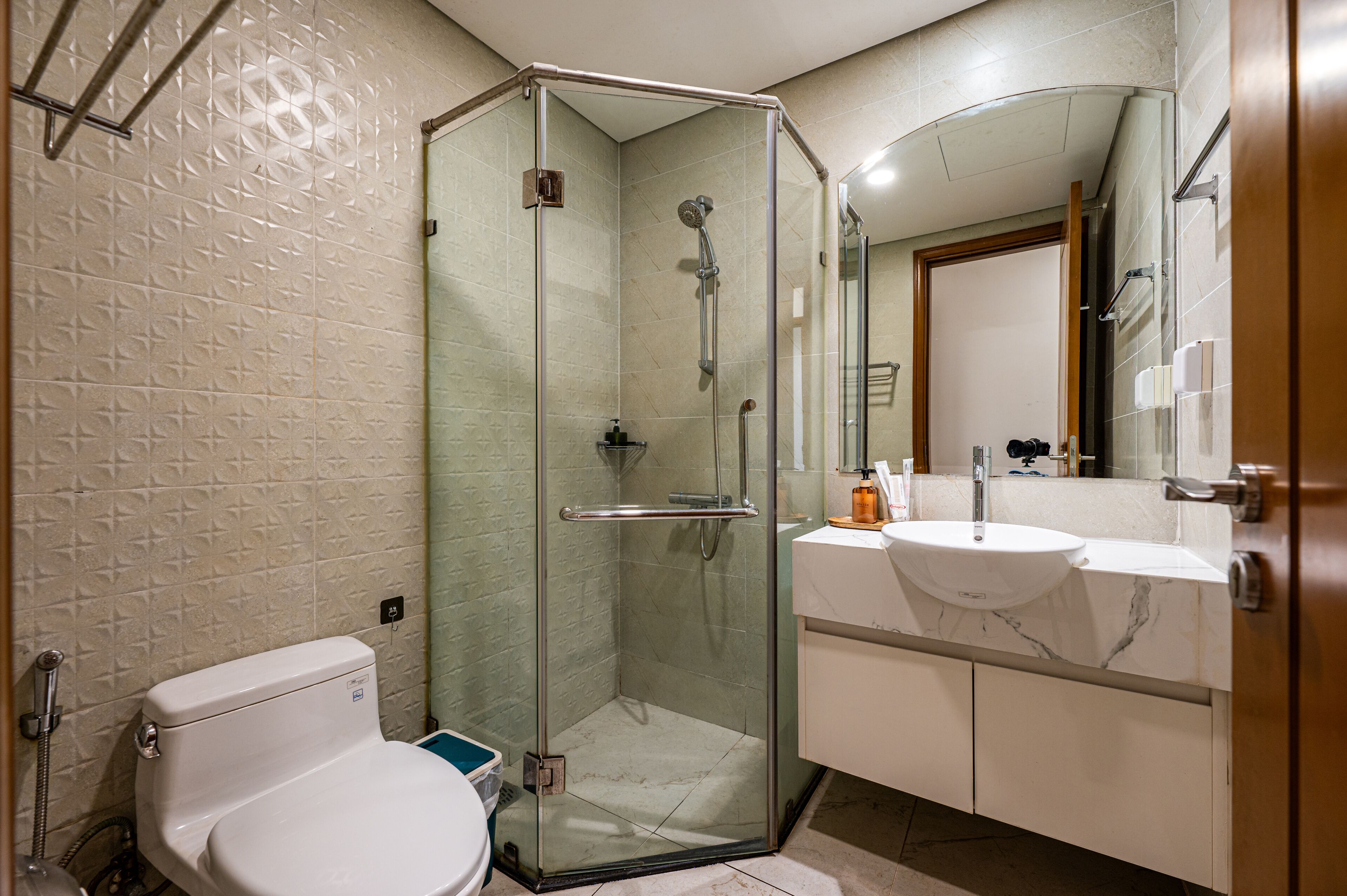 A bathroom with a glass-enclosed shower, a white toilet, and a marble sink.