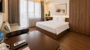 A hotel room with a bed, a desk with a chair, a TV, a wardrobe, and a window with curtains. - Danang Boutique Apartment | 02 Private Balcony 5 min to the Beach (Đà Nẵng)
