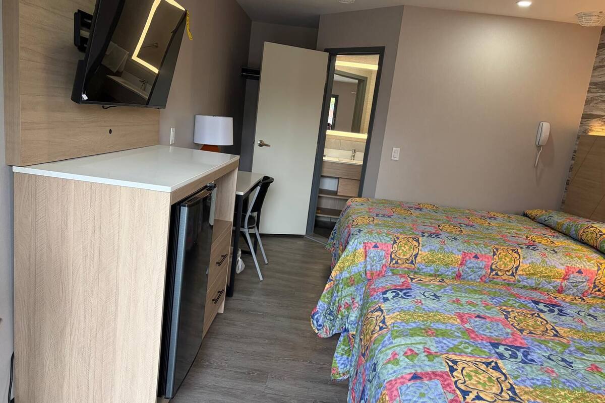 Una habitación de hotel compacta con cama, escritorio, silla, espejo y televisor.