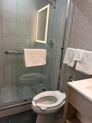 A modern bathroom with a glass shower enclosure, a toilet, and a sink with a mirror. - Midway Motel (Patchogue)