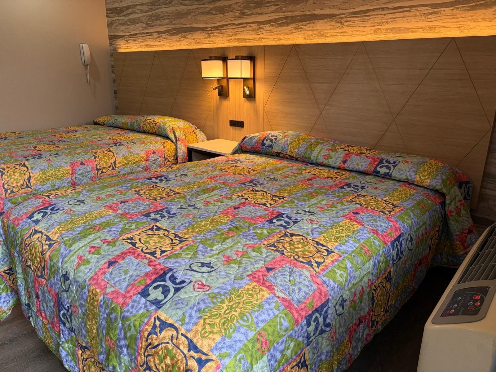 A hotel room with two beds, a wall-mounted phone, and a heater.