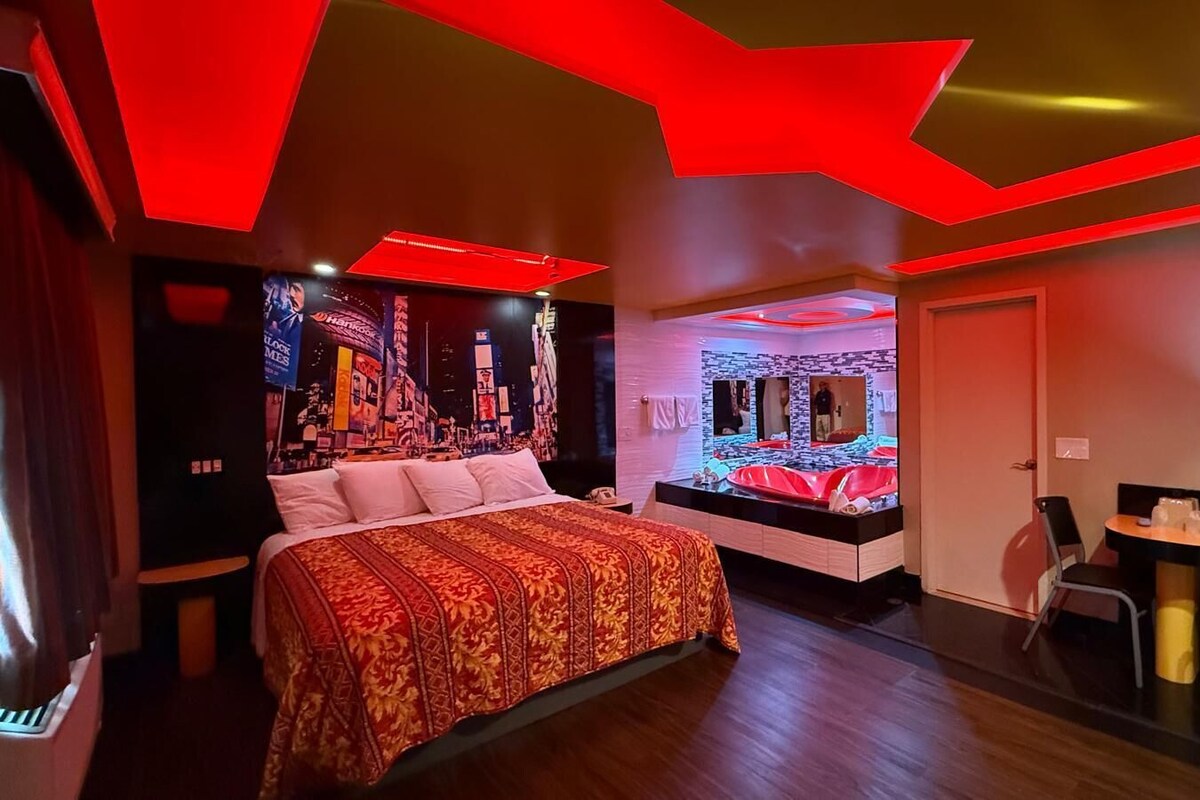 Una habitación de hotel moderna con una cama grande, una mesita, un espejo y una obra de arte original en la pared.