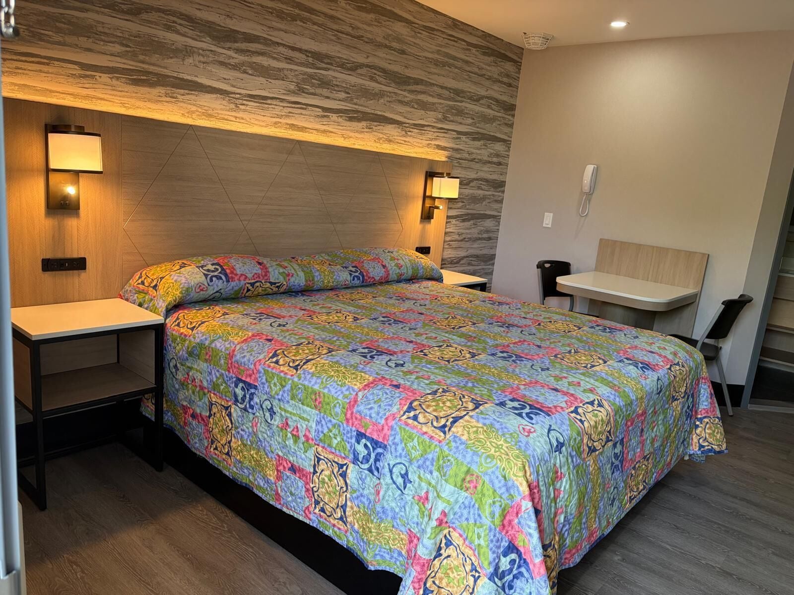 A hotel room with a bed, bedside tables, a desk, and a chair.