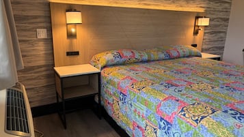 A bedroom with a patterned bedspread, two bedside lamps, a wooden headboard, and a small nightstand.