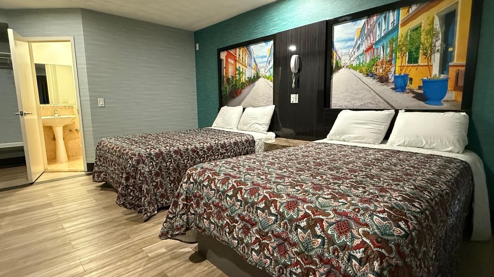 Habitación de hotel con dos camas, baño y una ventana grande con vistas a la ciudad.