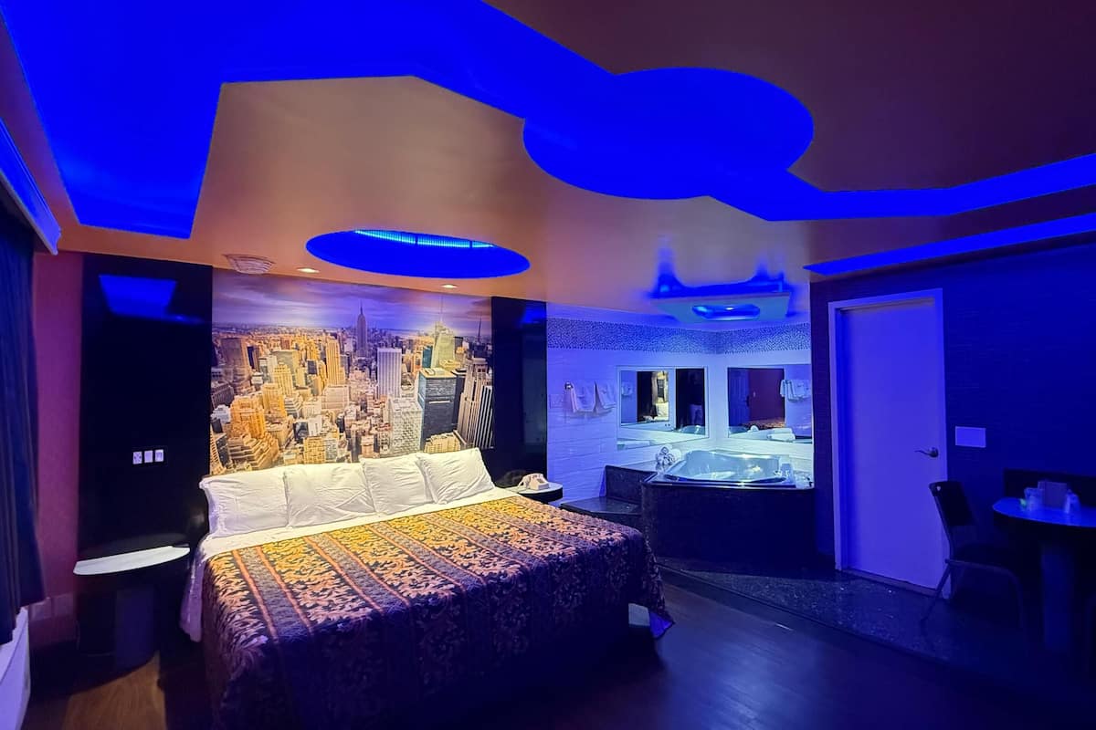 Una habitación de hotel moderna con un mural de paisaje urbano, una cama grande, una bañera y una pequeña mesa.