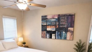 Ein Schlafzimmer mit Bett, Deckenventilator, einem Gemälde, einer kleinen Pflanze und einem Teppich.