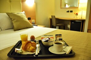 Un vassoio colazione con croissant, un bicchiere di succo d'arancia, una tazza di caffè e una piccola ciotola di cereali su un letto d'hotel.