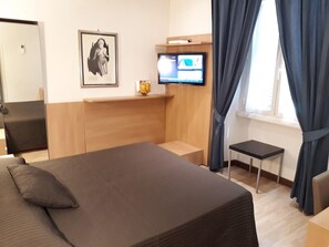 Hotellihuone, jossa on sänky, pieni pöytä, televisio ja ikkuna, jossa on verhot.