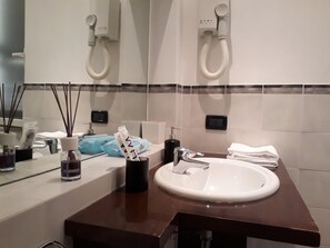 Un baño con un lavabo blanco, un espejo, un secador de pelo y un perchero para toallas.