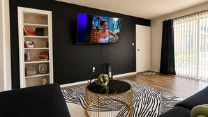 Un salon moderne avec un tapis à motifs noir et blanc, une table basse ronde, une bibliothèque et un téléviseur à écran plat fixé au mur.