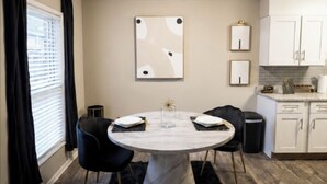 Un coin repas avec une table ronde, des chaises noires, un vase servant de centre de table et une cuisine en arrière-plan.