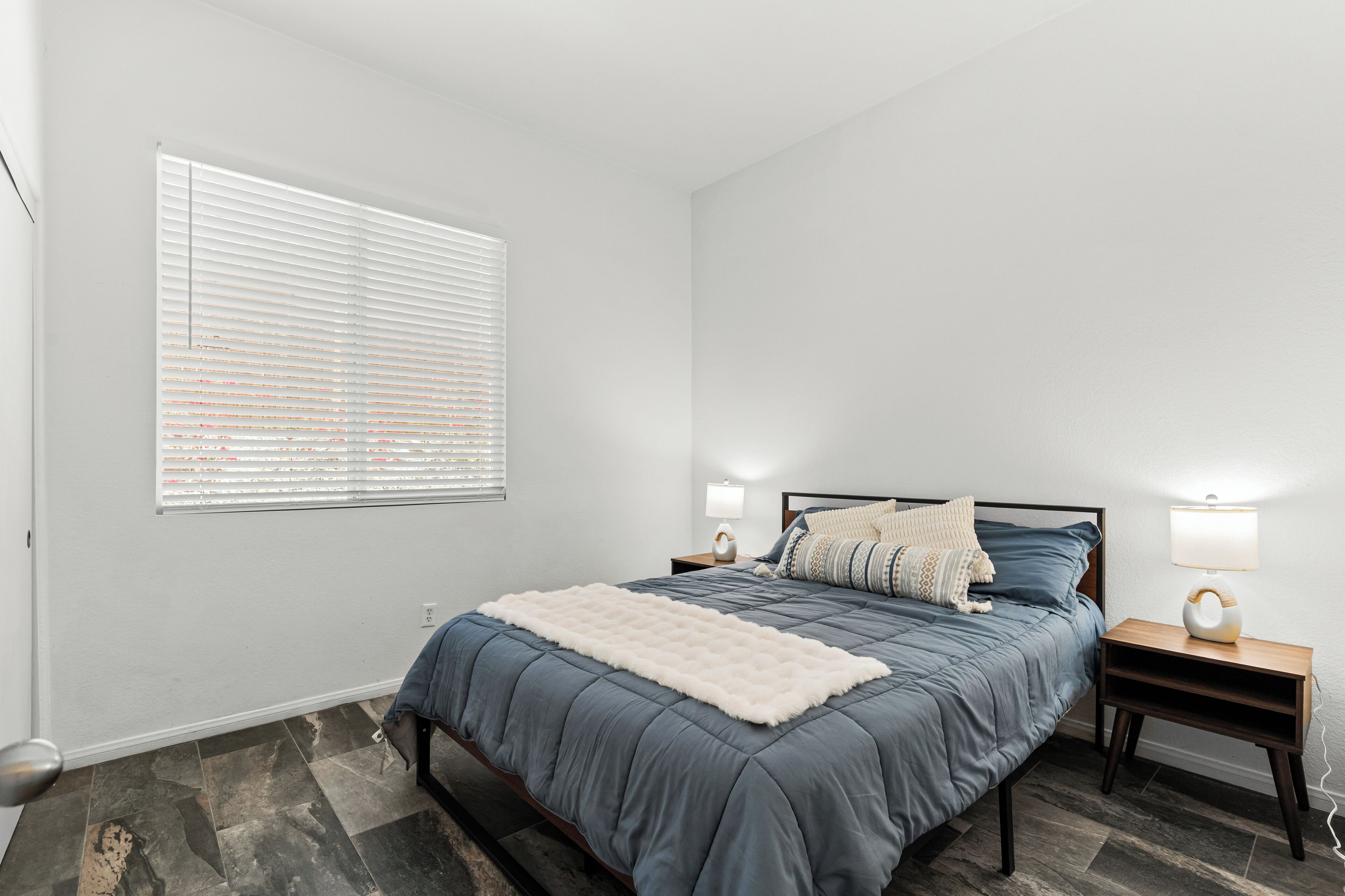 Une chambre à coucher avec un lit, des lampes de chevet, une fenêtre avec des stores et un tapis.