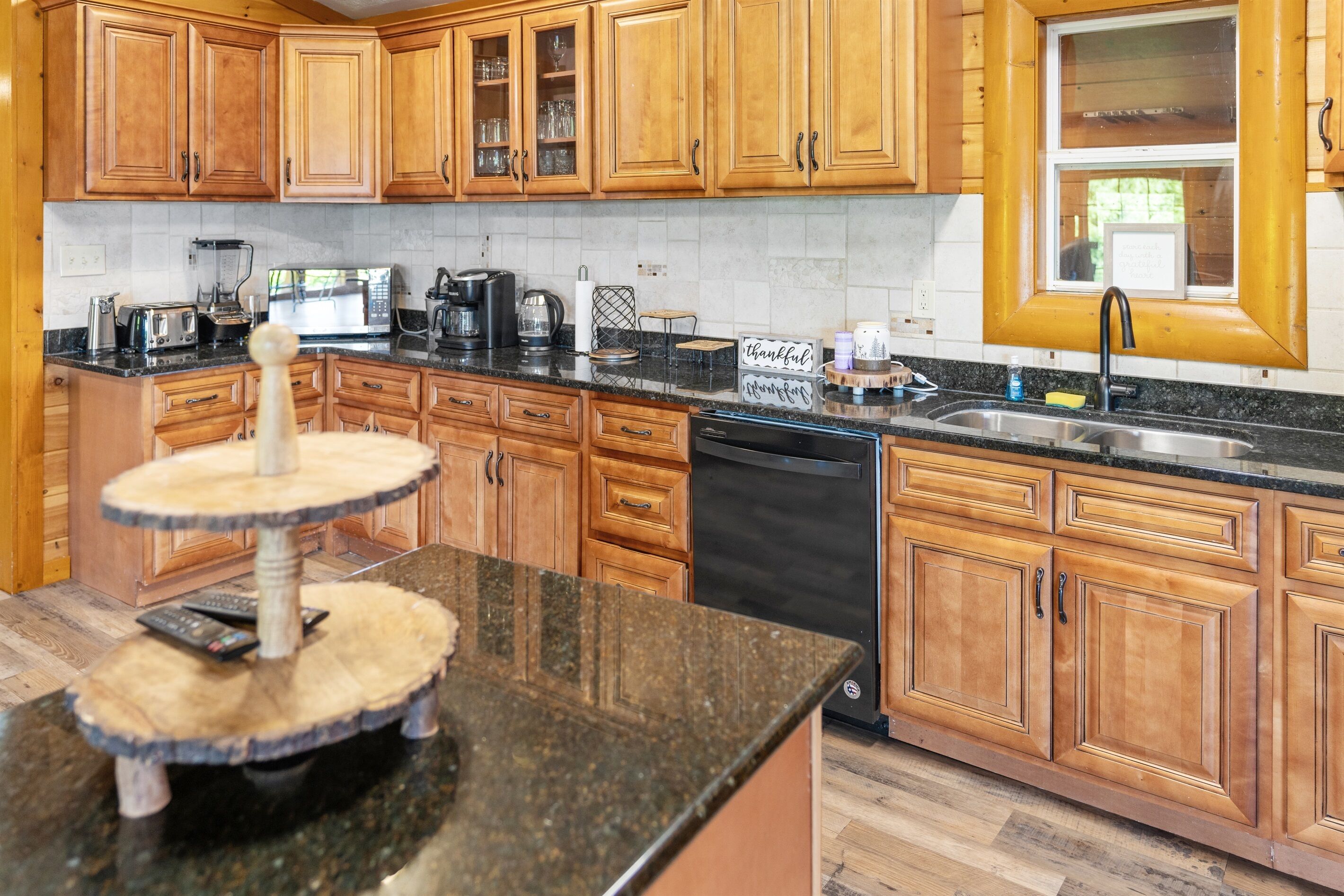 A kitchen with wooden cabinets, a black countertop, a blender, a toaster, a coffee maker, and a dish rack.