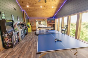 Ein Zimmer mit Tischtennisplatte, Spielautomaten und großen Fenstern mit Blick ins Freie.