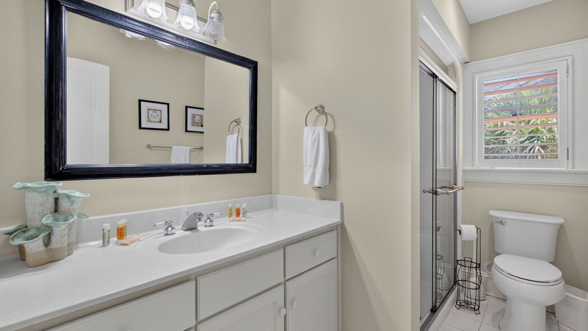 A bathroom with a large mirror, two sinks, a toilet, and a window with a view.