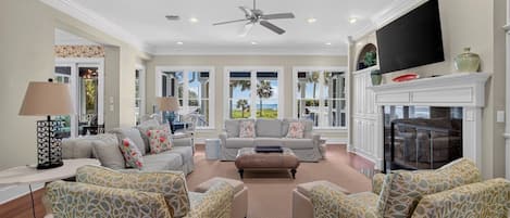 A spacious living room with a fireplace, comfortable seating, and large windows offering a view of the outdoors.