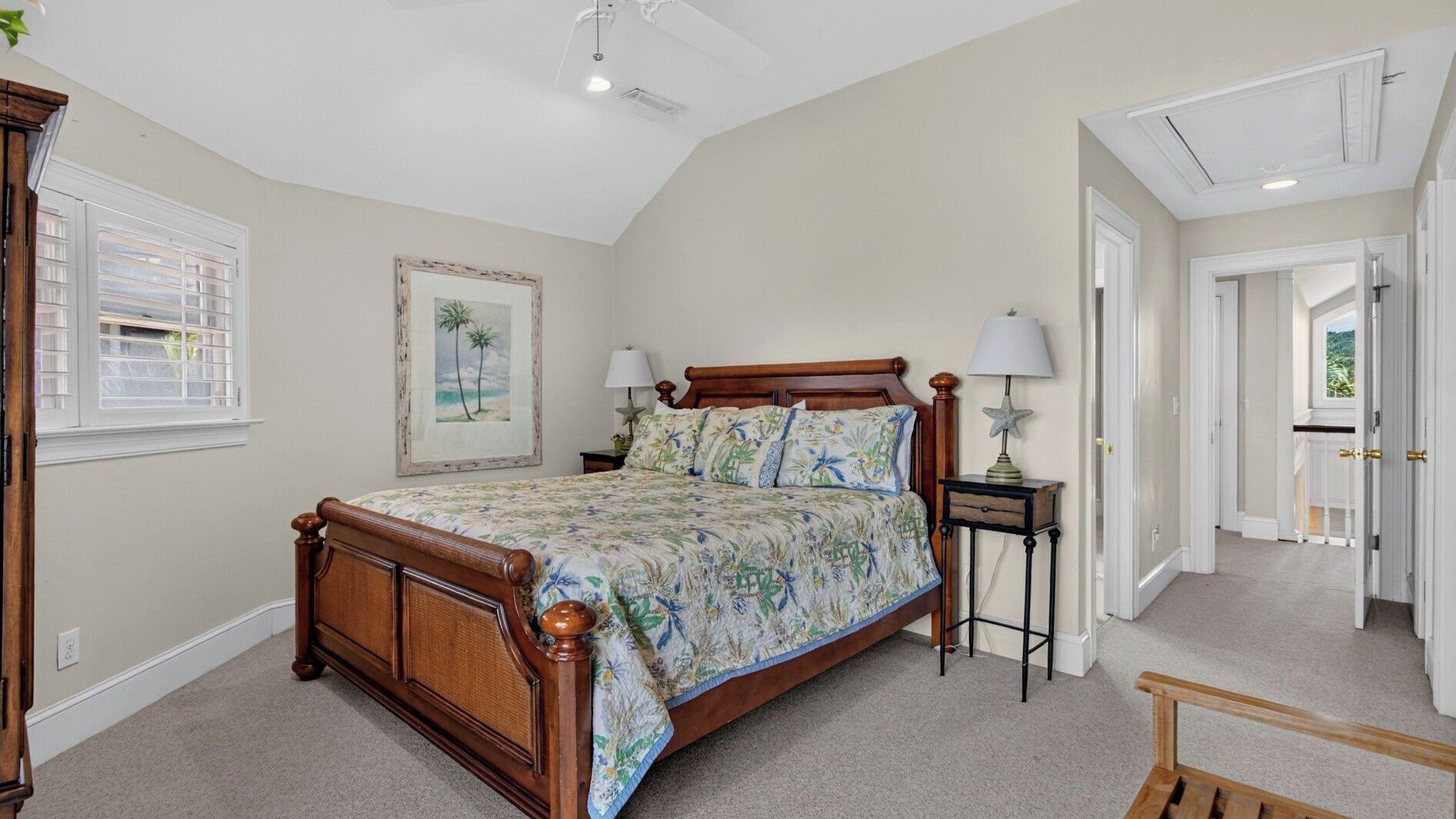 A bedroom with a large bed, a nightstand, a lamp, a framed picture, and a window with blinds.