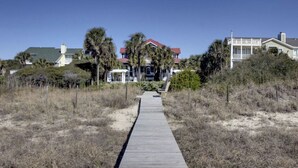 A wooden boardwalk leading to a house with a red roof, surrounded by dry grass and trees. - 3902 Palm Blvd by Avantstay Beach Access! Oceanfront Views w/ Pool (Isle of Palms)