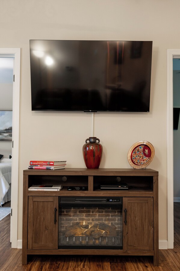 Un televisor montado en la pared sobre un mueble de madera con chimenea, libros y objetos decorativos.