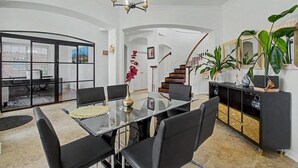 Uma sala de estar espaçosa com uma mesa de jantar de vidro, cadeiras pretas, uma escada e uma grande planta.