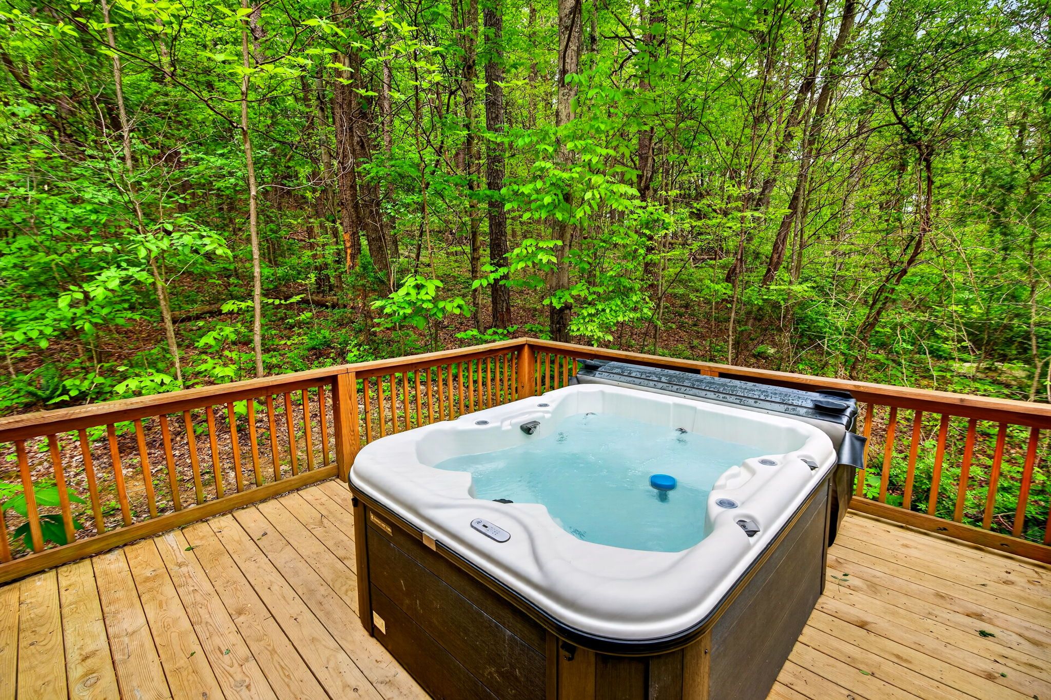A hot tub on a wooden deck surrounded by a forest.