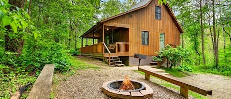 A wooden cabin with a porch, a fire pit, and a gravel path.
