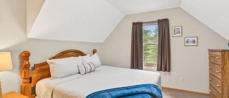 Una camera da letto con un letto, una cassettiera, un comodino, una lampada e una finestra con tende.