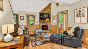 A living room with a stone fireplace, leather furniture, and a television. - Turkey Run, Cozy Woodland Cabin Retreat in the Heart of Hocking Hills, Hot Tub (Logan)