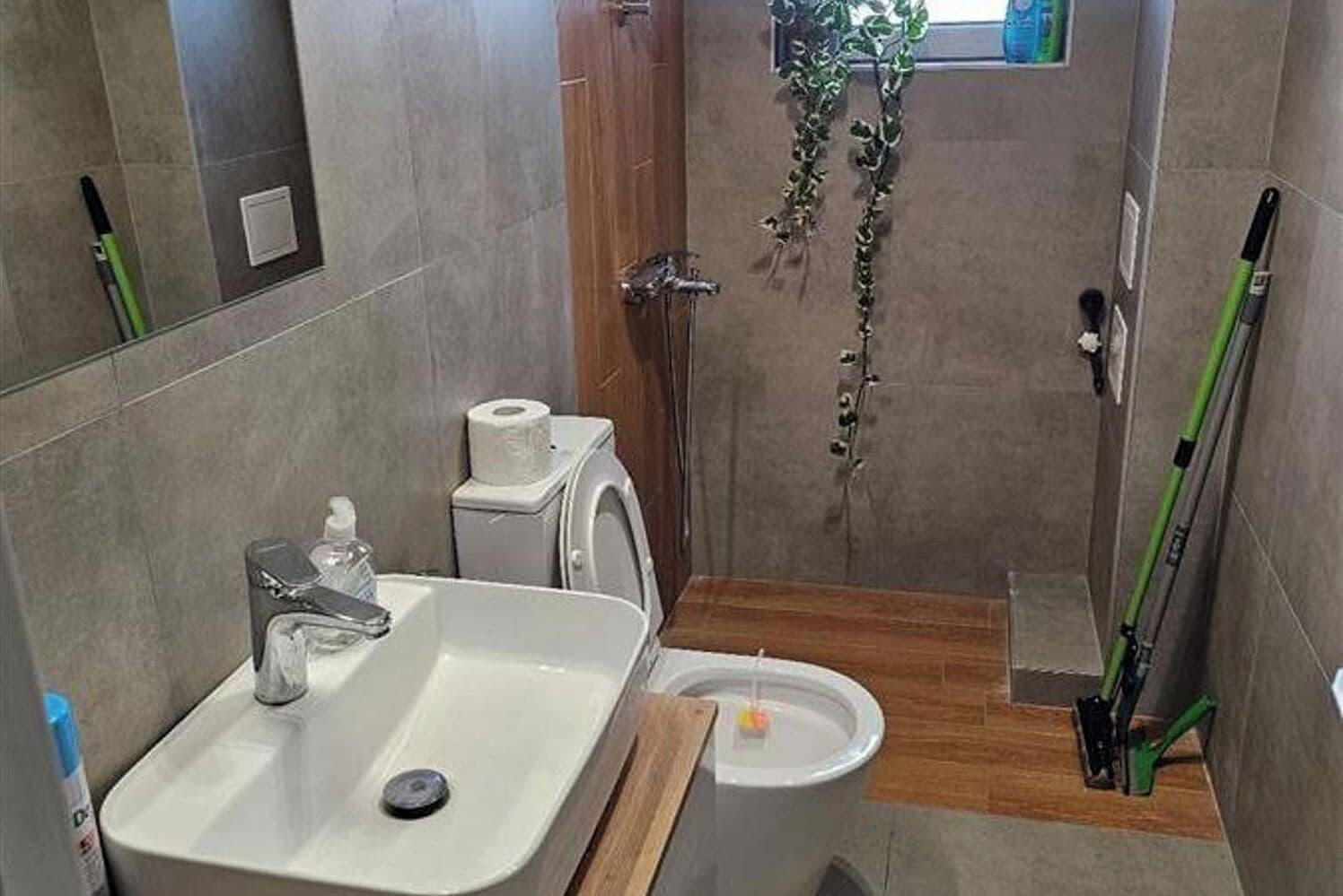Et badeværelse med vask, toilet, bruser og et lille vindue med planter.