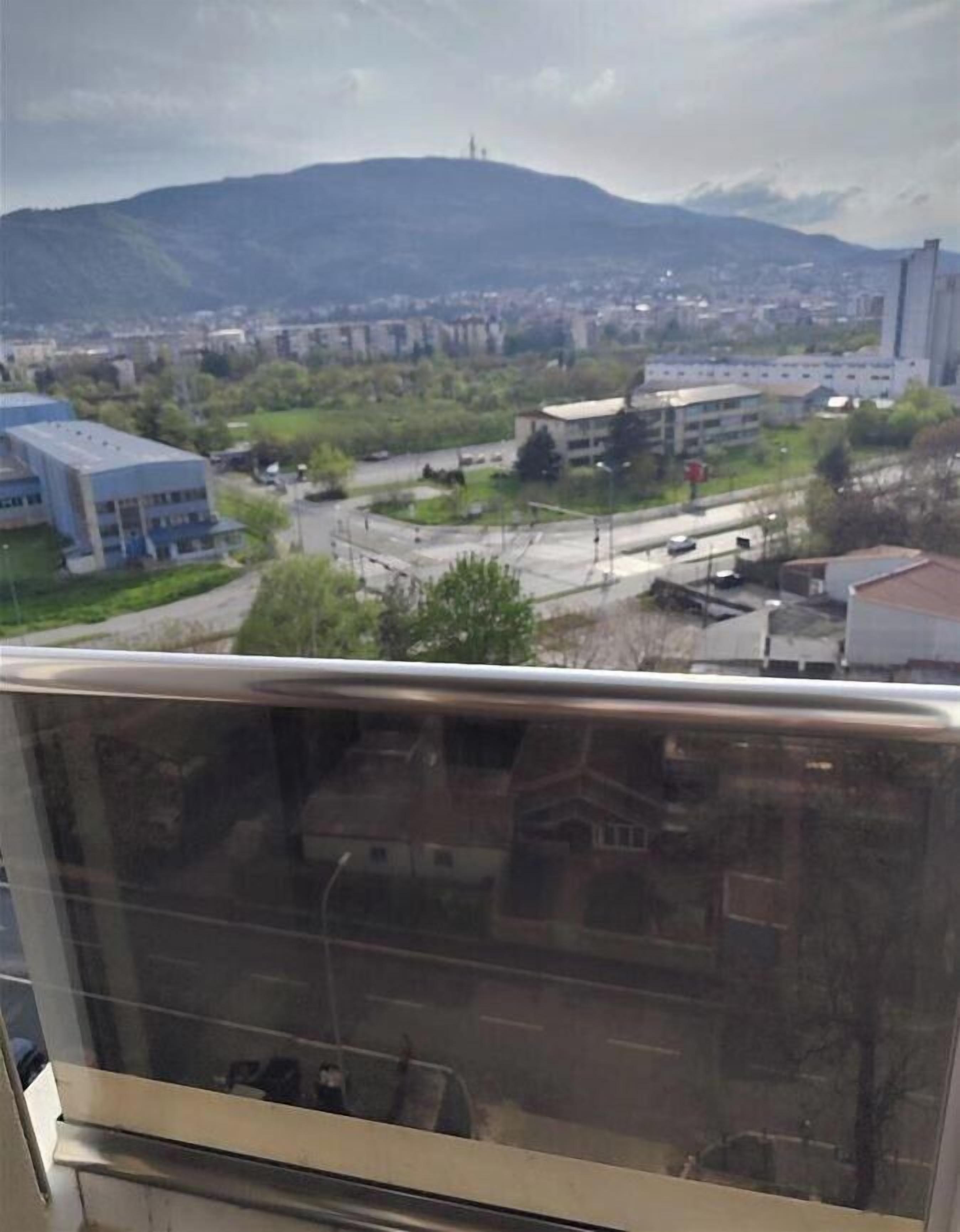 Eine Stadtlandschaft mit Bergen im Hintergrund, eine Straße mit Fahrzeugen und Gebäuden.