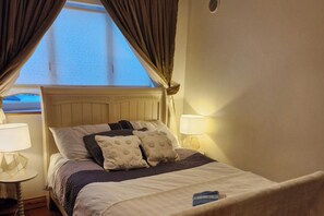 Una cama con cabecera, dos lámparas de noche y una ventana con cortinas.