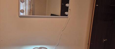 Une pièce avec un miroir de coiffeuse, une lampe et une porte.