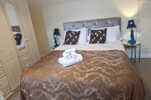 Une chambre d’hôtel avec un lit, des oreillers, une table de chevet, une lampe et un miroir.